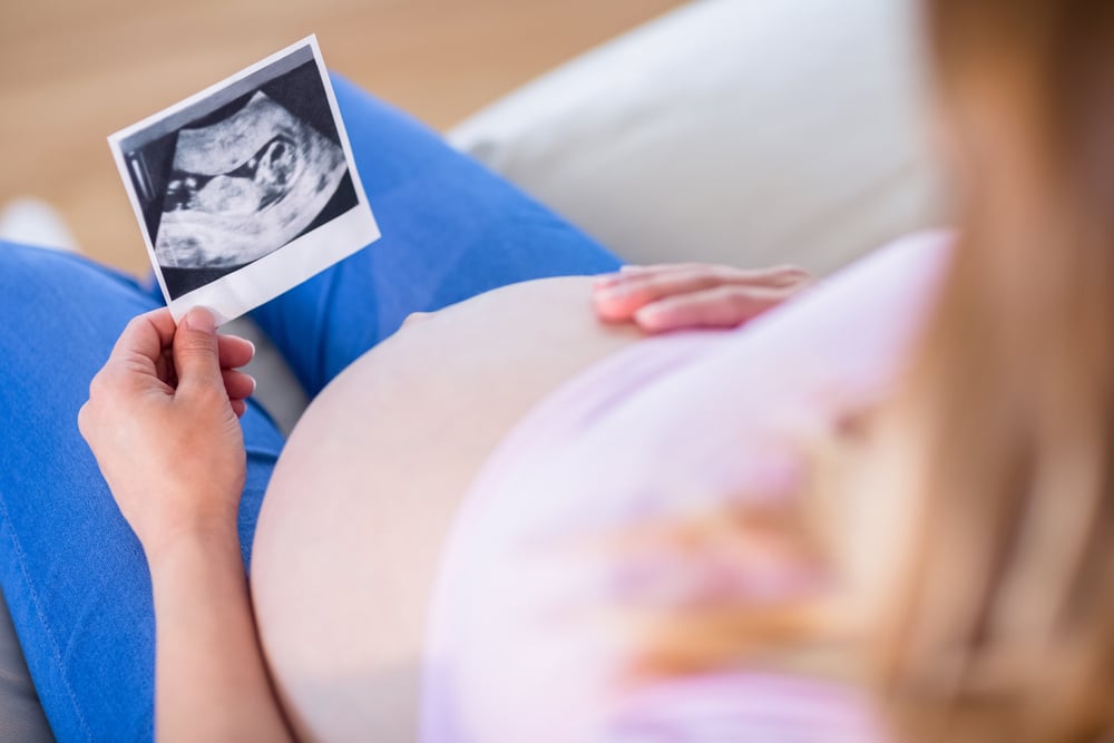 Pregnant woman looking at ultrasound scans and touching her belly in the living room