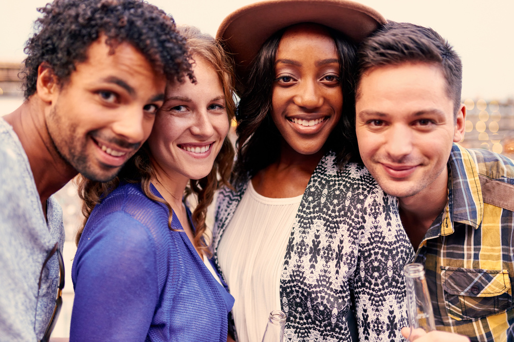 Multi-ethnic millenial group of friends taking a selfie photo with mobile phone on rooftop terrasse at sunset